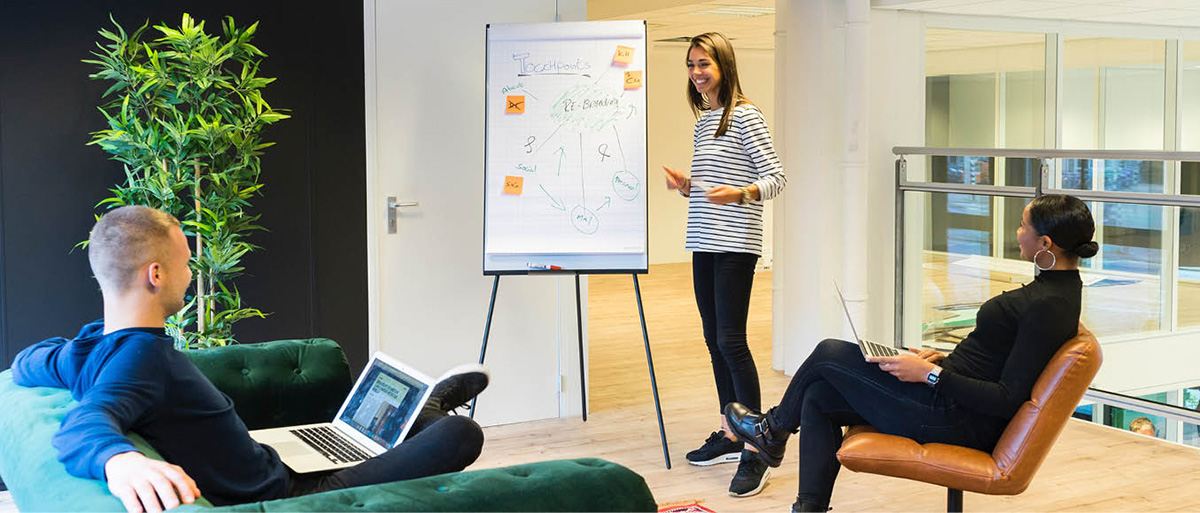 a standing woman presenting informationon a whiteboard to a couple sitting down