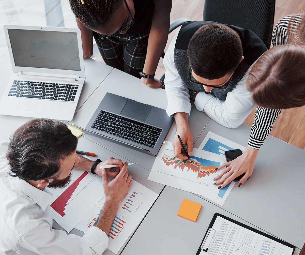 People gathered around a table with laptops, charts, and paper, working together