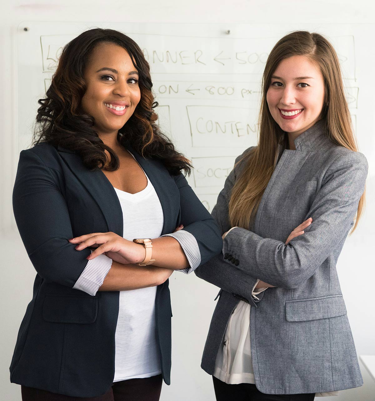 two women in business attire standing next to each other with their arms crossed and smiling