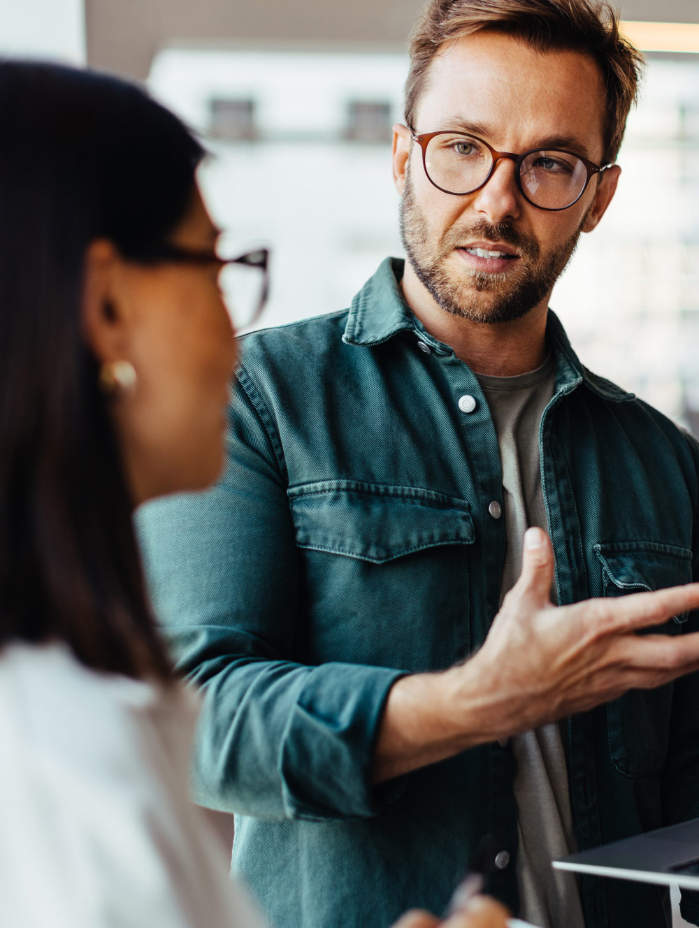 man with glasses and denim jacket talking to woman wearing glasses and gold earrings